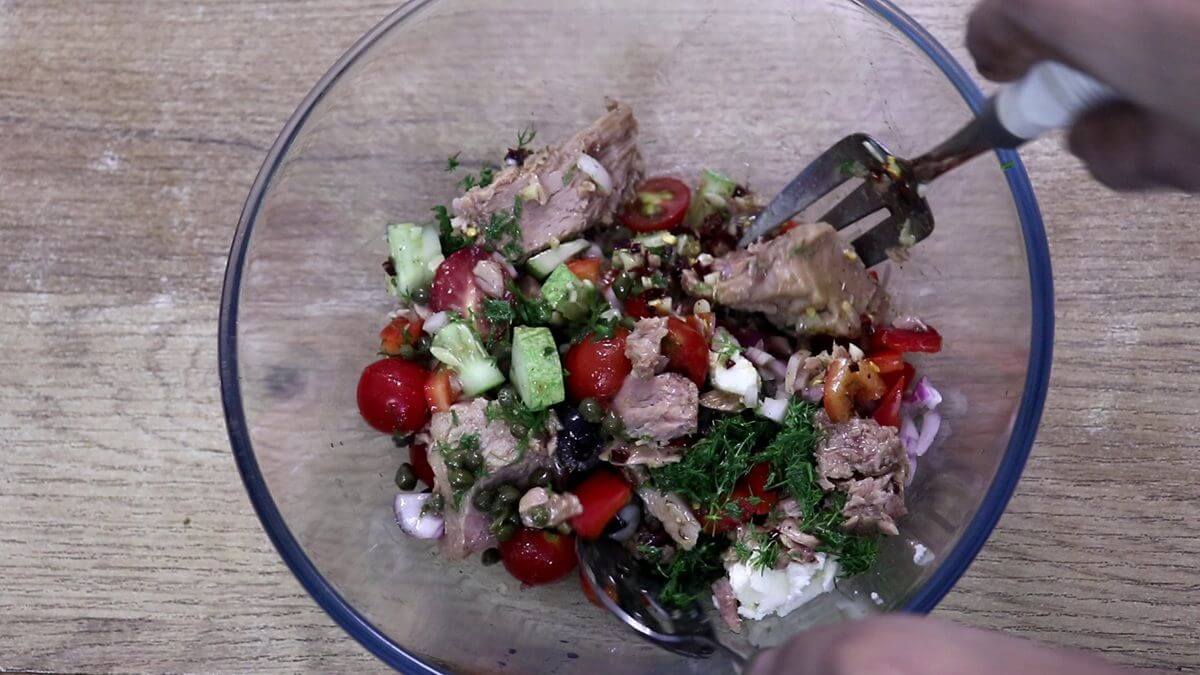 Mediterranean tuna salad being gently tossed with lemon olive oil dressing until evenly coated.