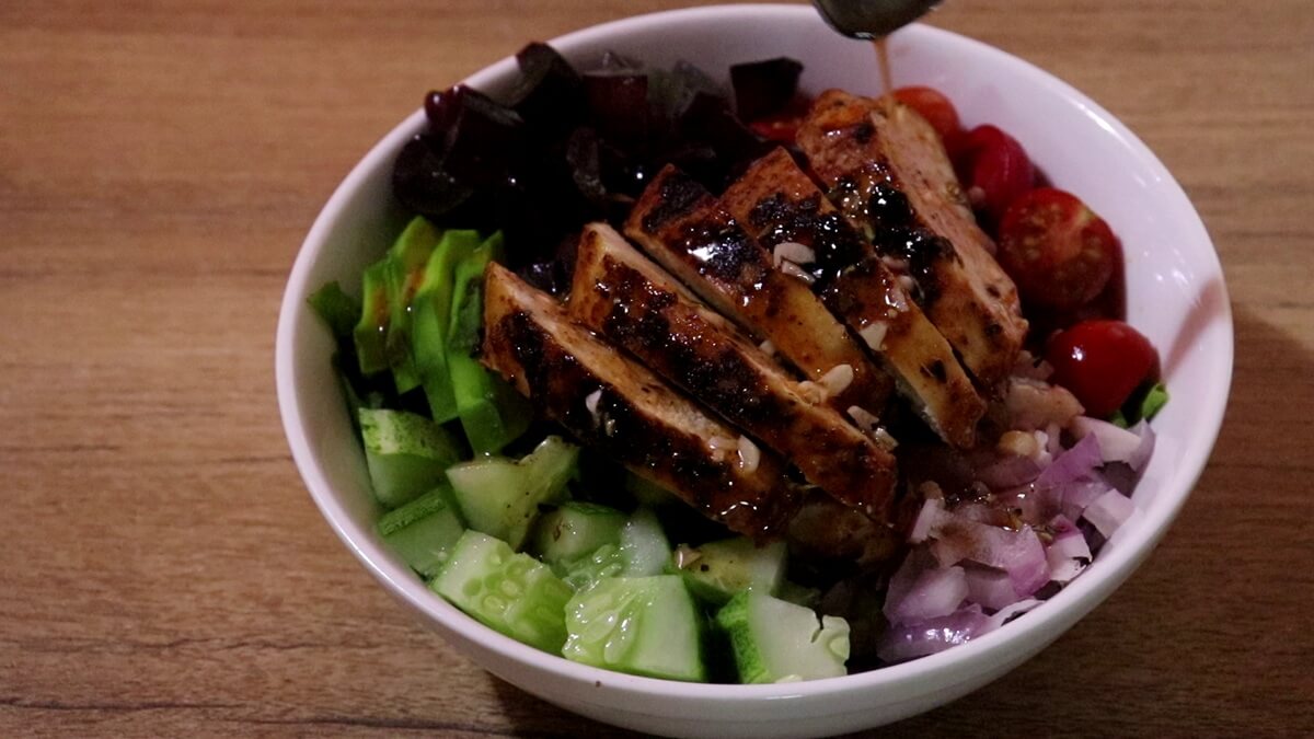 poring dressing over grilled chicken avocado salad in a bowl.