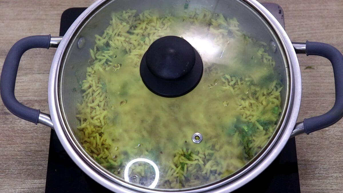 Stirring fresh cilantro into fluffy turmeric rice after cooking.