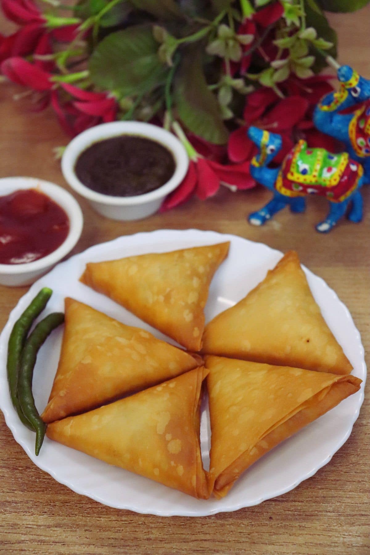Five crispy chicken keema samosas served on a white plate with tomato ketchup and green chutney on the side.