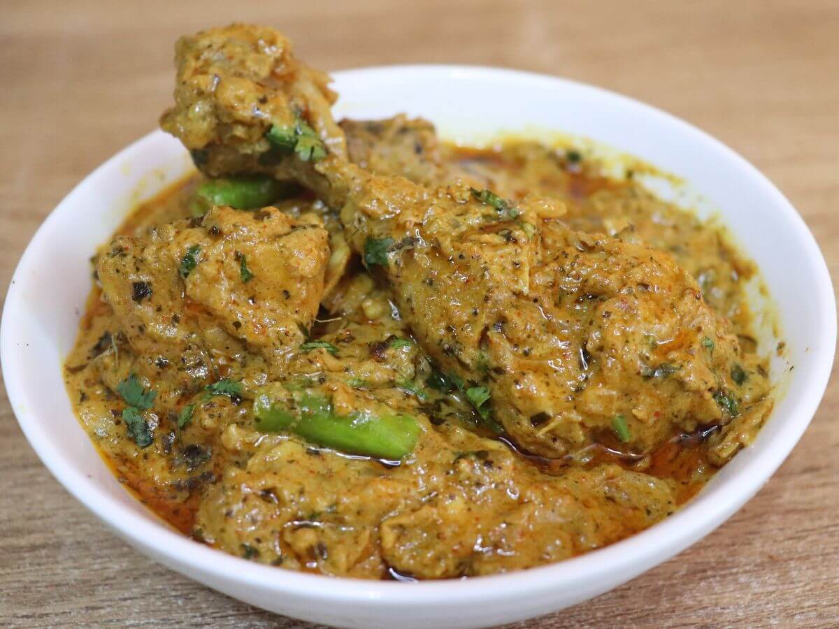 Dahi chicken curry served in a white bowl over brown countertop.