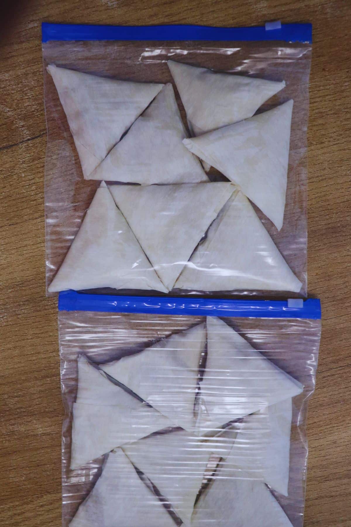 Frozen uncooked chicken keema samosas arranged in a single layer in zip lock bag.