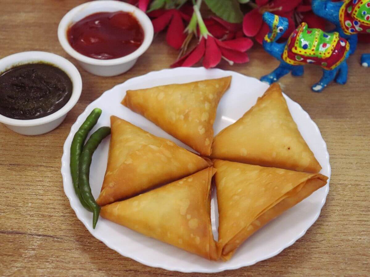 Crispy chicken keema samosas served with green chilies, green chutney and tomato ketchup.