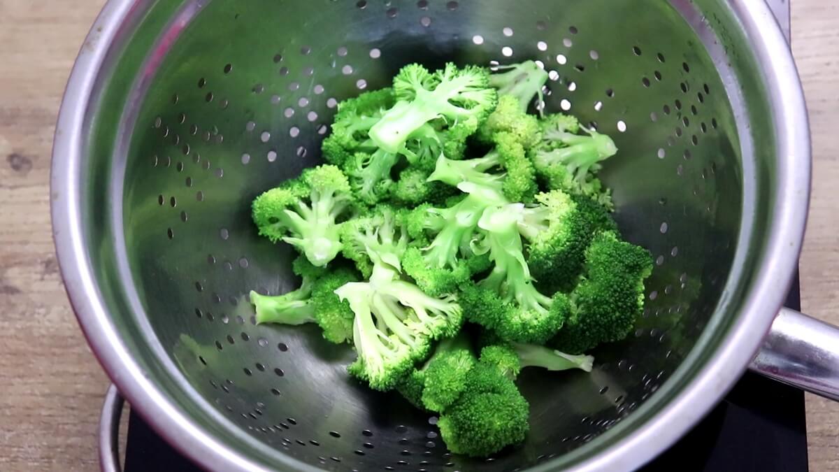 Broccoli florets steaming in a colander over a pot of water for lemon garlic broccoli.