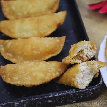 Karanji with coconut rava filling, one cut open and served on a black plate.