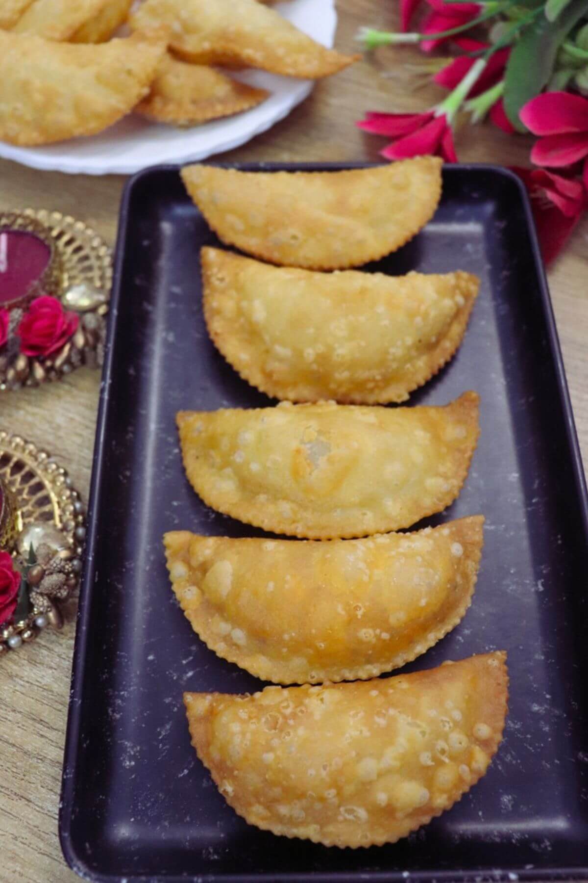 Maharashtrian karanji served on a black plate, with more karanji on a plate beside it.