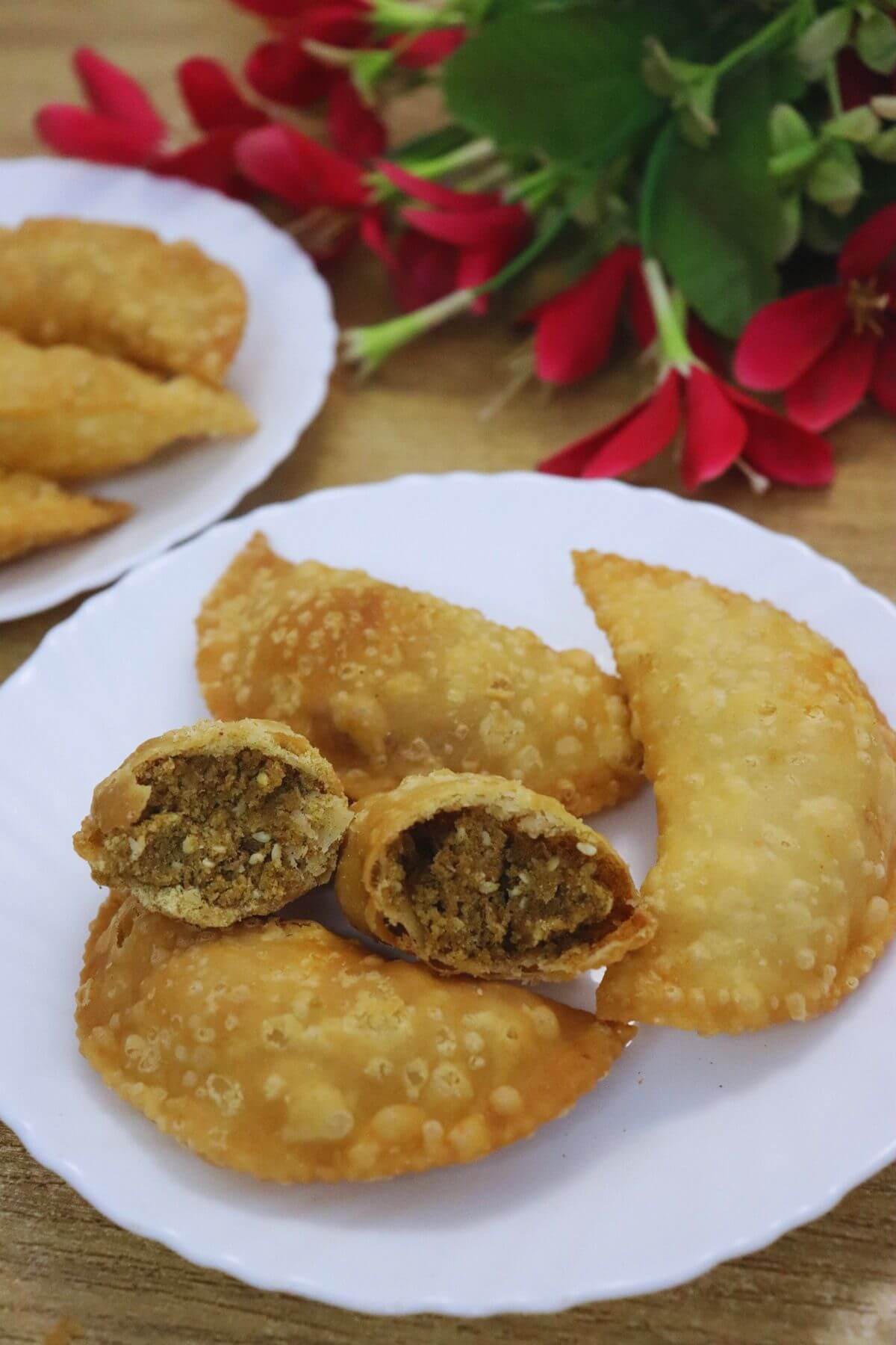 Goan Pittachyo Neureo arranged on a plate, with one broken open to show the sweet moong dal filling.