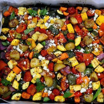 close-up of mediterranean oven roasted vegetables in a baking sheet. Garnished with Feta cheese and basil leaves.