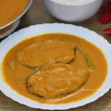 close-up of kingfish curry served on a white plate with a bowl full of rice on the side.